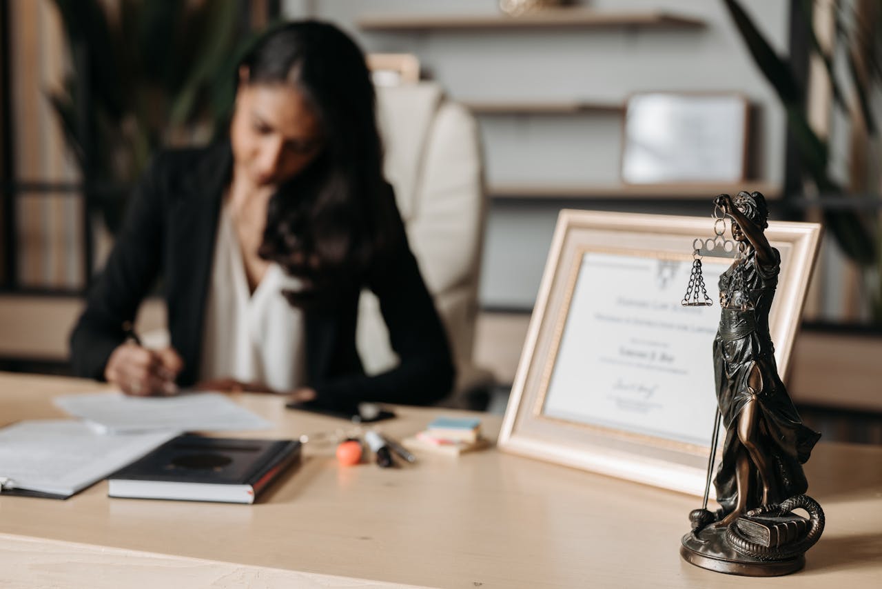 fitness-service-01 Focused woman writing at desk with Lady Justice figurine and certificate in office.